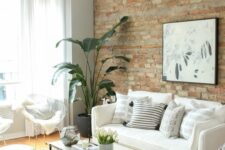 25 a neutral living room with a brick accent wall, neutral seating furniture, a coffee table, a black chandelier and a potted plant