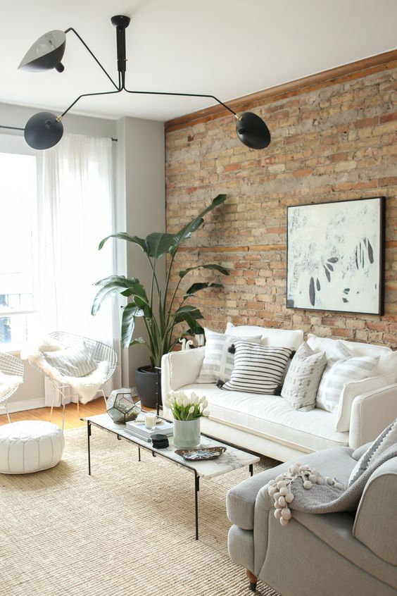a neutral living room with a brick accent wall, neutral seating furniture, a coffee table, a black chandelier and a potted plant