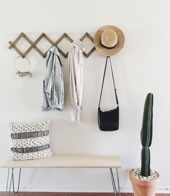 a boho entryway with a hairpin leg bench, a rack, a pillow and a potted cactus is a cool and lovely space