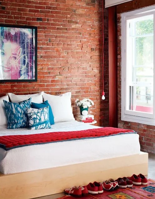 a bright contemporary bedroom with a comfy bed, a hanging bulb and an exposed brick statement wall that takes over the whole space