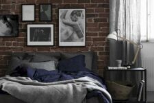 33 a chic moody bedroom with a faux brick wall, a cork bench, a dark bed and a monochromatic gallery wall