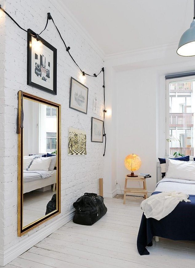 a dreamy Scandinavian bedroom with a white brick wall, a whitewashed floor shows off black framed art and dark bedding
