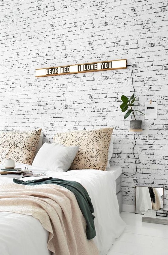a Nordic bedroom with a whitewashed brick wall, a grey bed, lights and plants is a stylish and welcoming space
