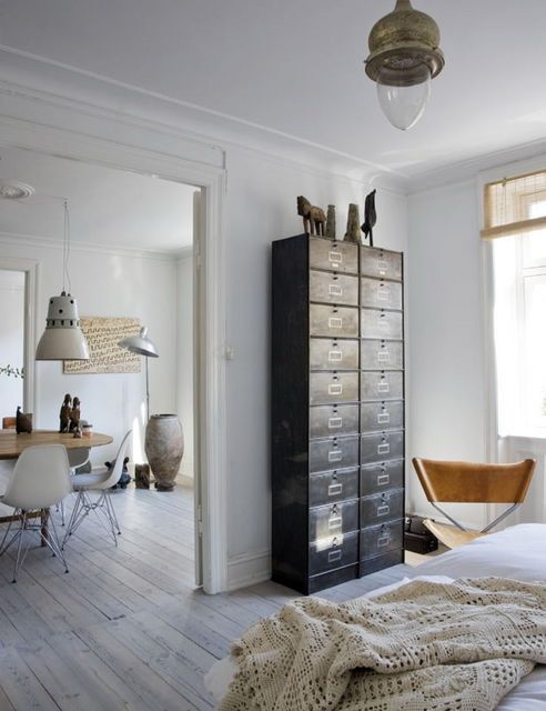 a light-filled Scandinavian space with a dark card cabinet that is used instead of a usual dresser and a leather chair