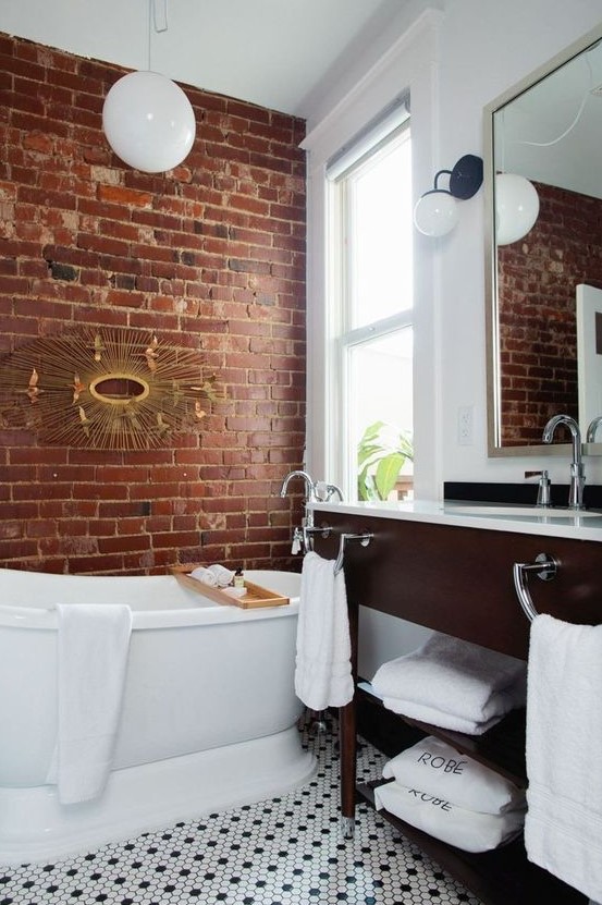 a chic bathroom done in white and with contrasting touches - a red brick wall and a rich toned vanity