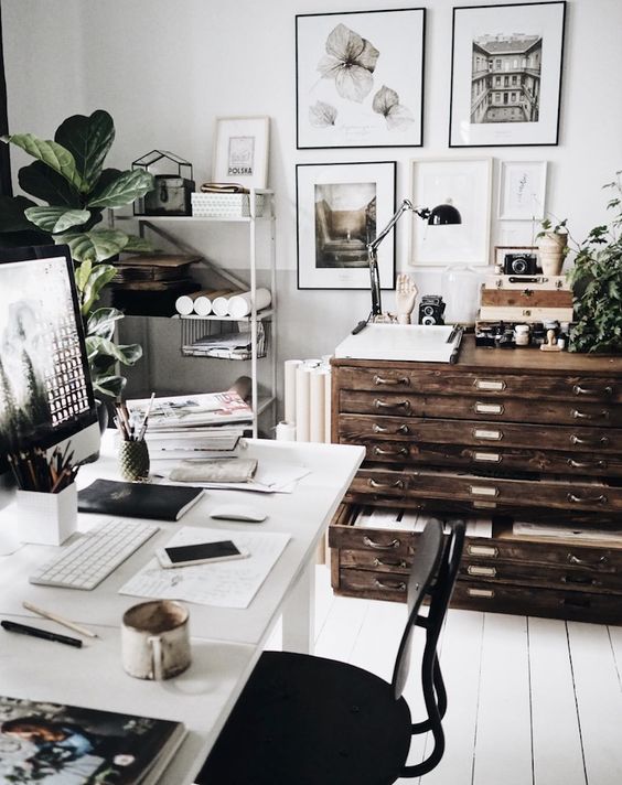 a Scandinavian home office in neutrals, with a white desk and a black chair, a white shelving unit, a stained file cabinet for storage and black and white gallery wall