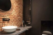 46 a moody and chic bathroom in black with a single red brick wall that makes the space stand out
