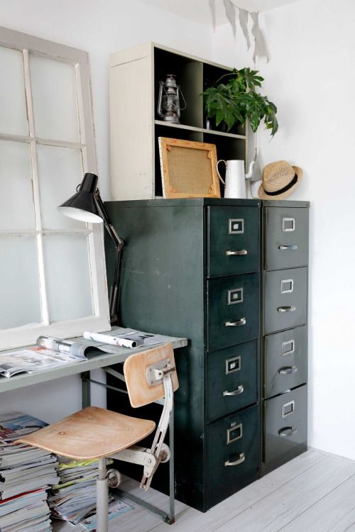 a vintage industrial home office with a metal desk and a plywood chair, a black card cabinet for storage, a table lamp and some greenery