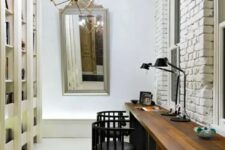 50 a neutral home office with a large shelving unit, a textural white brick wall, a large stained shared desk, black chairs, a mirror and a chandelier