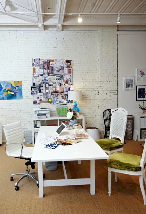 a neutral home office with a white brick wall, a shelving unit, a large shared desk, mismatching chairs, a memo board and some lights