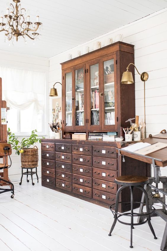 a vintage working space with a stained card cabinet and a glass one on top, a vintage industrial desk and some stools