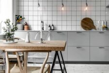 a Nordic kitchen with grey cabinets, a white tile backsplash, sconces that hold bulbs, a table with a cork countertop and wooden chairs