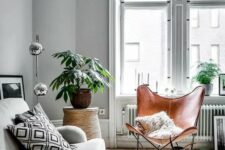 a Nordic living room with a grey sofa and printed pillows, a brown leather butterfly chair, a printed rug, potted greenery