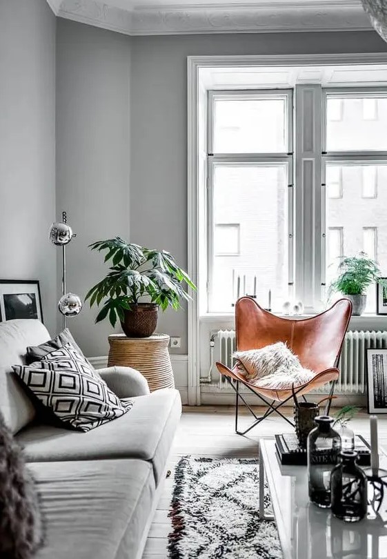 a Nordic living room with a grey sofa and printed pillows, a brown leather butterfly chair, a printed rug, potted greenery