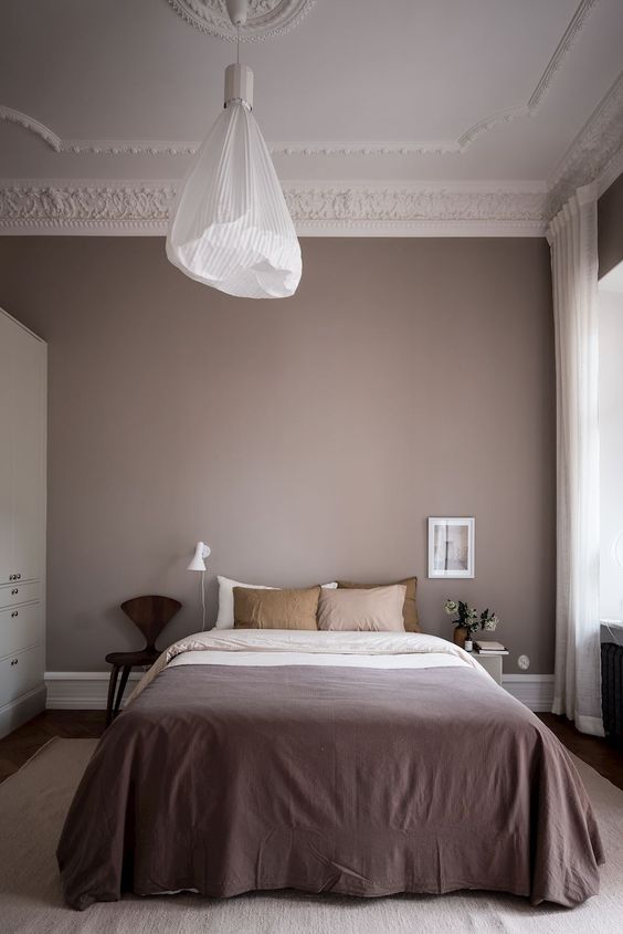 a Scandinavian bedroom with mauve walls, a bed with mauve and mustard bedding, mismatching nightstands and a pendant lamp