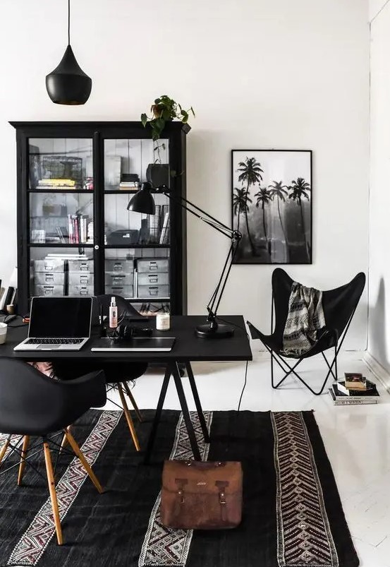 a Scandinavian dining room with a black bookcase, a black desk and chairs, a black butterfly chair and some lamps plus a printed rug