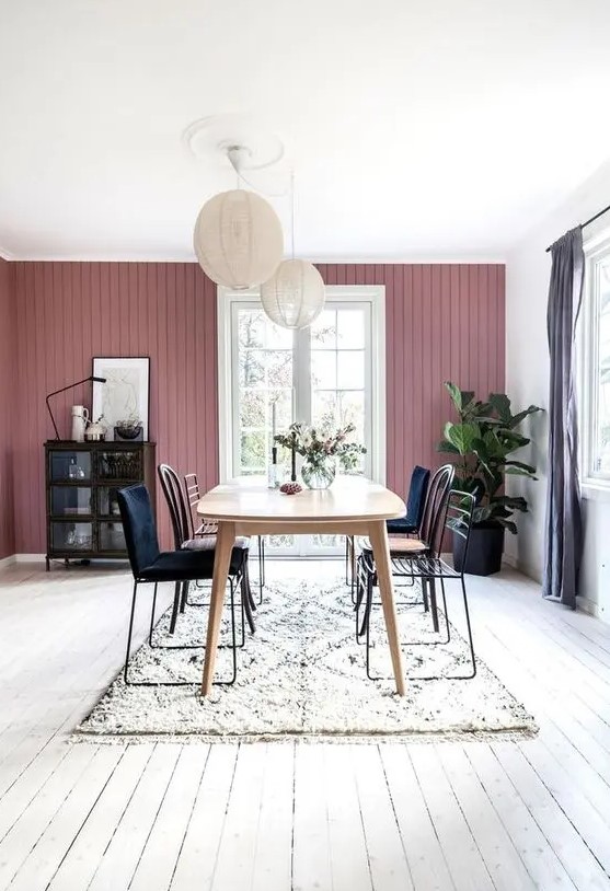 a Scandinavian dining room with a mauve wall, a wooden table, mismatching chairs, paper lamps and a dark buffet