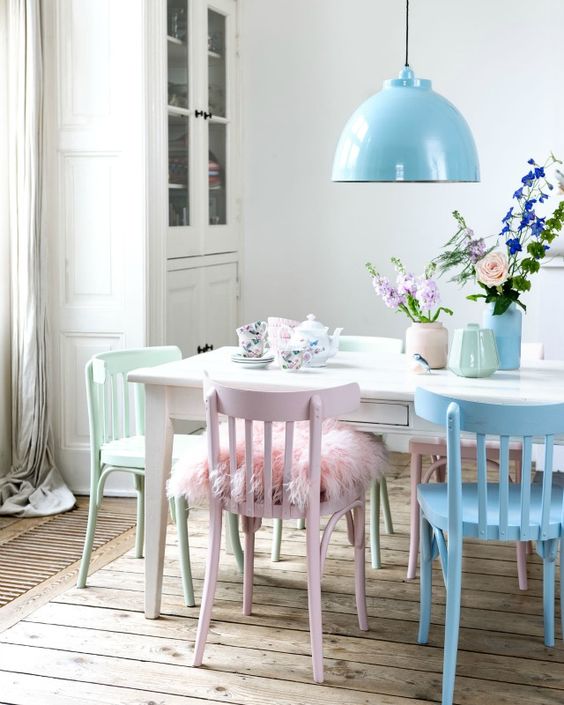 a Scandinavian dining room with a neutral storage unit, a white table, pastel chairs and a blue pendant lamp plus pastel vases