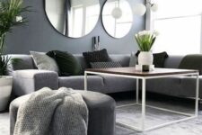 a Scandinavian living room with a grey sectional, a grey pouf and a blanket, black pillows and a duo of round mirrors
