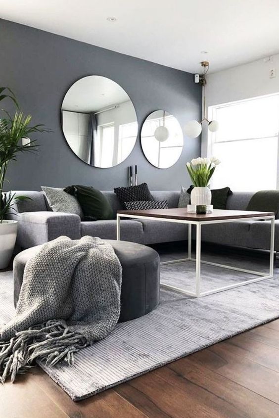 a Scandinavian living room with a grey sectional, a grey pouf and a blanket, black pillows and a duo of round mirrors