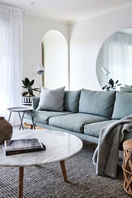 a Scandinavian living room with a grey sectional, a low coffee table, a side table, a large round mirror and some plants