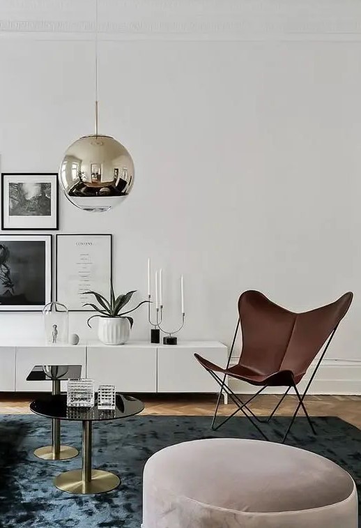 a Scandinavian living room with an IKEA TV unit, a gallery wall, a brown leather butterfly chair, a blue rug and coffee tables