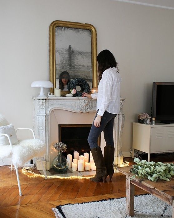 a beautiful French fireplace styled with candles, with a large vintage mirror and simple Scandinavian furniture around
