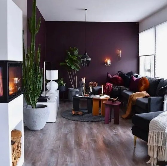 a beautiful contemporary living room with a deep purple accent wall, a black sofa and a chair, colorful coffee tables, potted plants and a fireplace