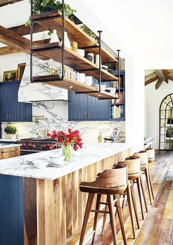 a beautiful kitchen with navy and stained cabinets, wooden beams, suspended shelves over the kitchen island and plywood stools