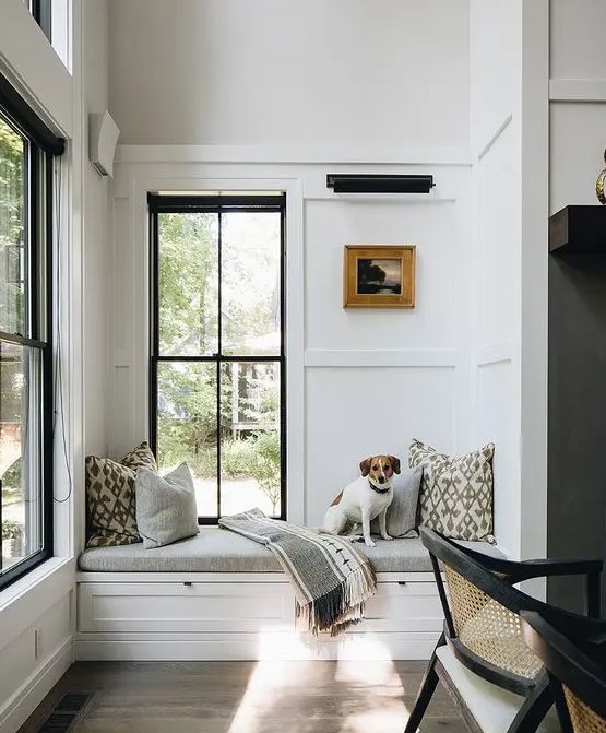 a beautiful neutral modern space with trim on the walls, two black double-hung windows, a built-in windowsill daybed and printed pillows