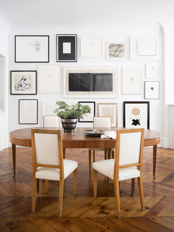 a beautiful vintage-inspired dining room with a black and white floor to ceiling gallery wall, an oval table and neutral chairs