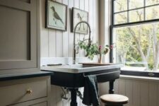 a beautiful vintage space with tan beadboard and cabinetry, black and white tiles, a black French double-hung window, a sink on a black stand