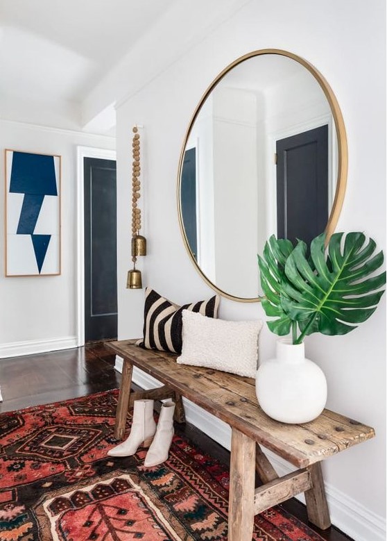 a boho chic entryway with a wooden bench, a boho rug, a wood frame round mirror plus bells hanging