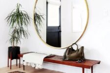 a boho chic entryway with a wooden bench, an oversized gold frame mirror, a boho rug and a potted plant