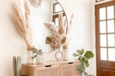 a boho entryway with a rattan console table, a round mirror, pampas grass and greenery, a printed rug