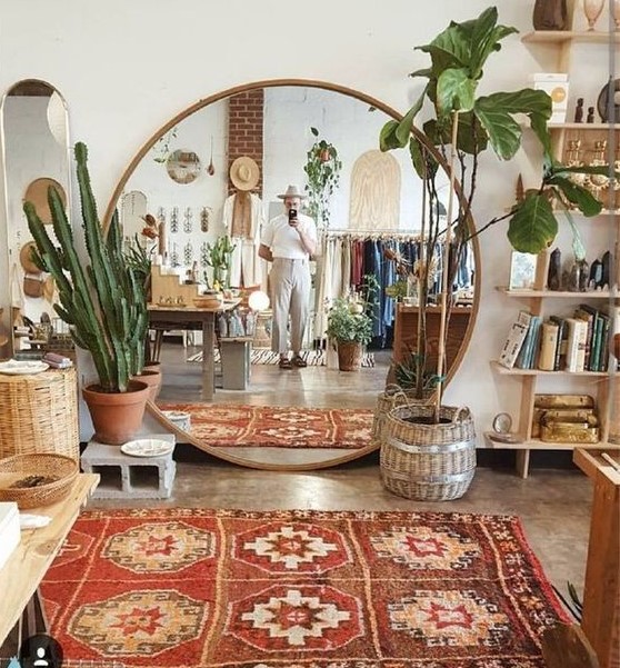 a boho living room with wooden and wicker furniture, potted plants, a boho rug and an oversized round mirror
