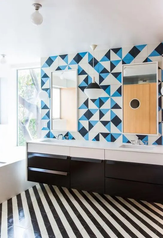 a bold bathroom with a striped black and white tile floor, a black vanity, white appliances, a blue, black and white tile wall