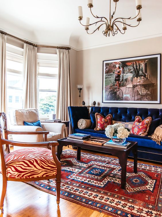 a bold living room with a navy sofa, a black coffee table, a neutral and an antique printed chair, a printed rug is cool