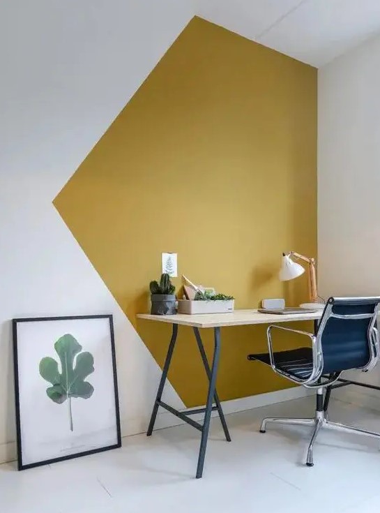 a bold modern working nook with a mustard and white color block wall, a lightweight desk, a black chair and a greenery print