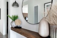 a breezy entryway with a built-in console, a round mirror, some vases and grasses is a small yet catchy space