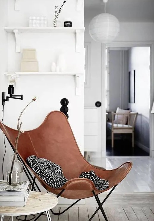 a brown leather butterfly chair styled with a black and white blanket, with some decor around for an awkward nook