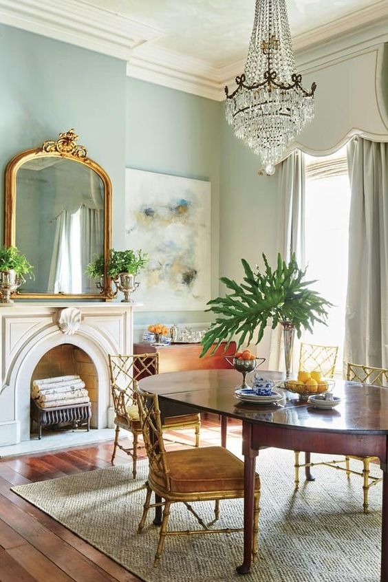 a catchy and refined living room with blue walls, a non-working fireplace, an oval table and antique chairs, a large crystal chandelier