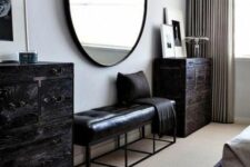 a catchy bedroom with a dark-stained bed and neutral bedding, a black leather bench, dark-stained dressers and an oversized mirror