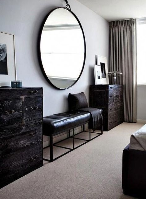 a catchy bedroom with a dark-stained bed and neutral bedding, a black leather bench, dark-stained dressers and an oversized mirror