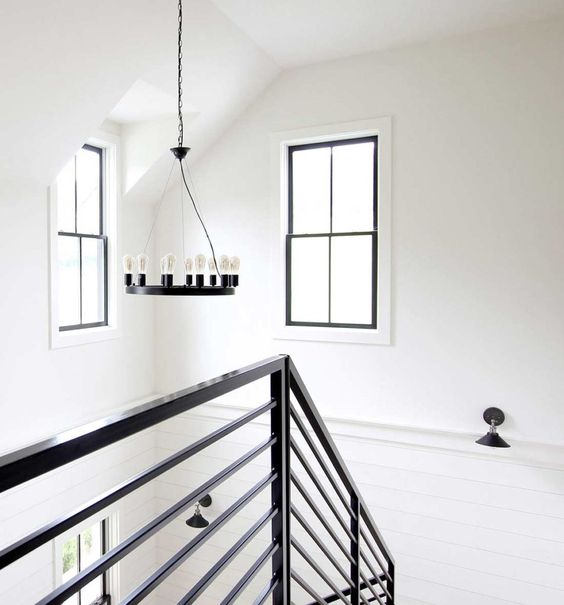 a catchy black and white farmhouse space with paneling and black touches - double-hung windows, railing and a chandelier