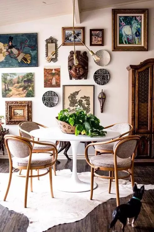 a catchy dining room with a round table and vintage chairs, a rug, a free form gallery wall and a cool chandelier