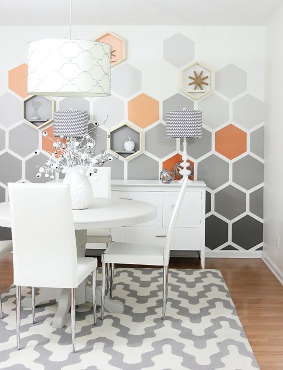 a catchy dining space with a hexagon accent wall, white furniture, a printed rug, coral and gold touches