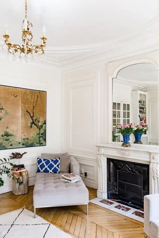 a chic Parisian nook with a grey daybed, a French fireplace and a mirror over it, a parquet floor, an oversized artwork