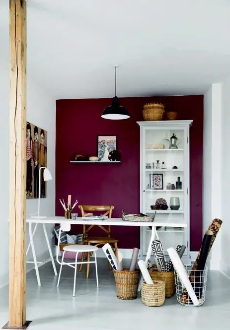 a chic craft room with a purple accent wall, white furniture, baskets with posters and artworks and a black pendant lamp plus a wooden beam