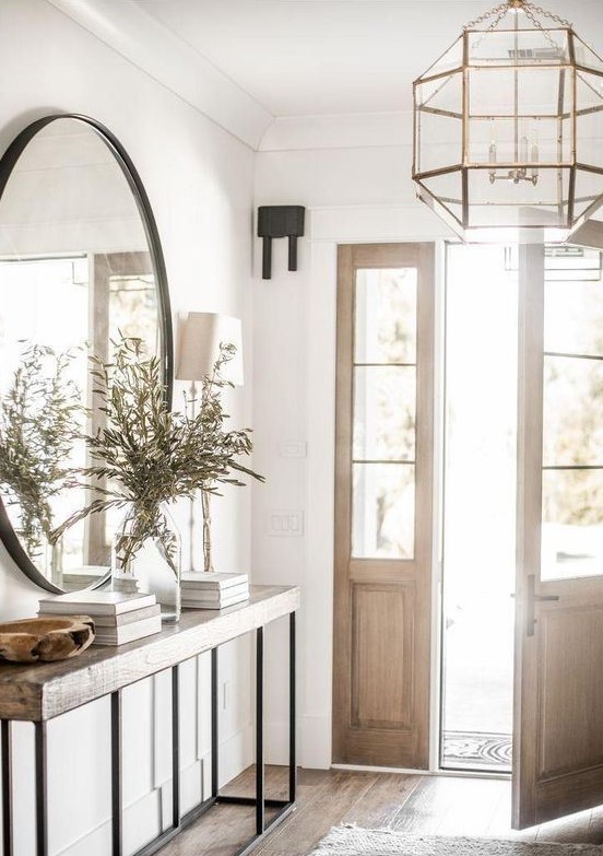 a chic farmhouse entryway with a wooden and metal console, a catchy faceted chandelier and a round mirror
